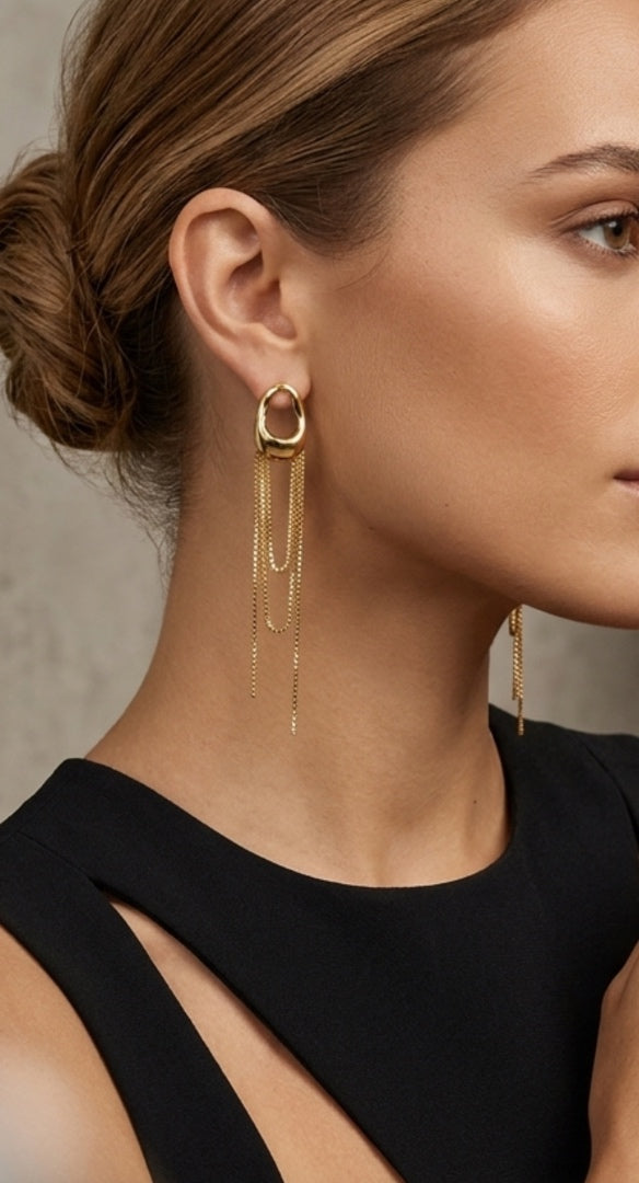 Close-up of a person wearing gold hoop earrings with dangling chains against a neutral background.