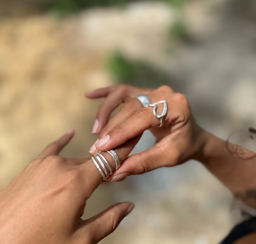 Two hands with silver rings on a blurred natural background