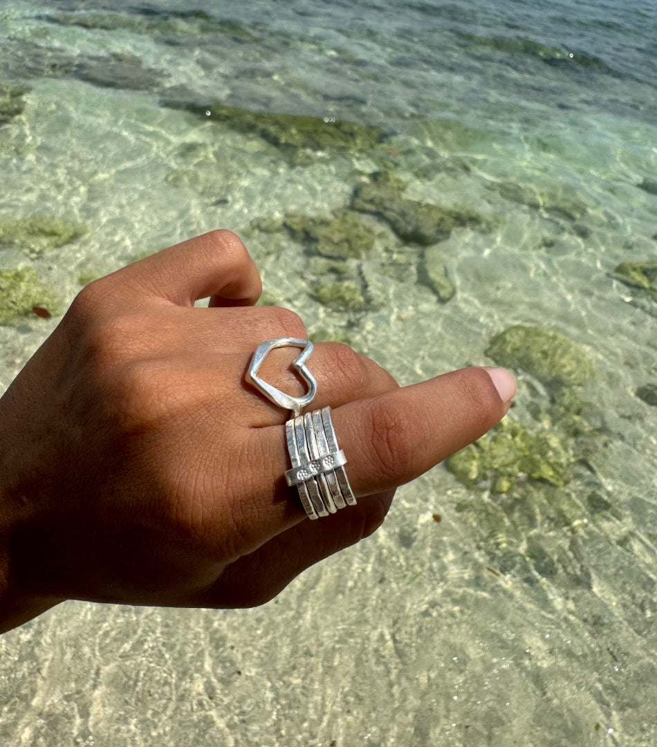 Hand wearing a silver ring with a heart design against a clear water background