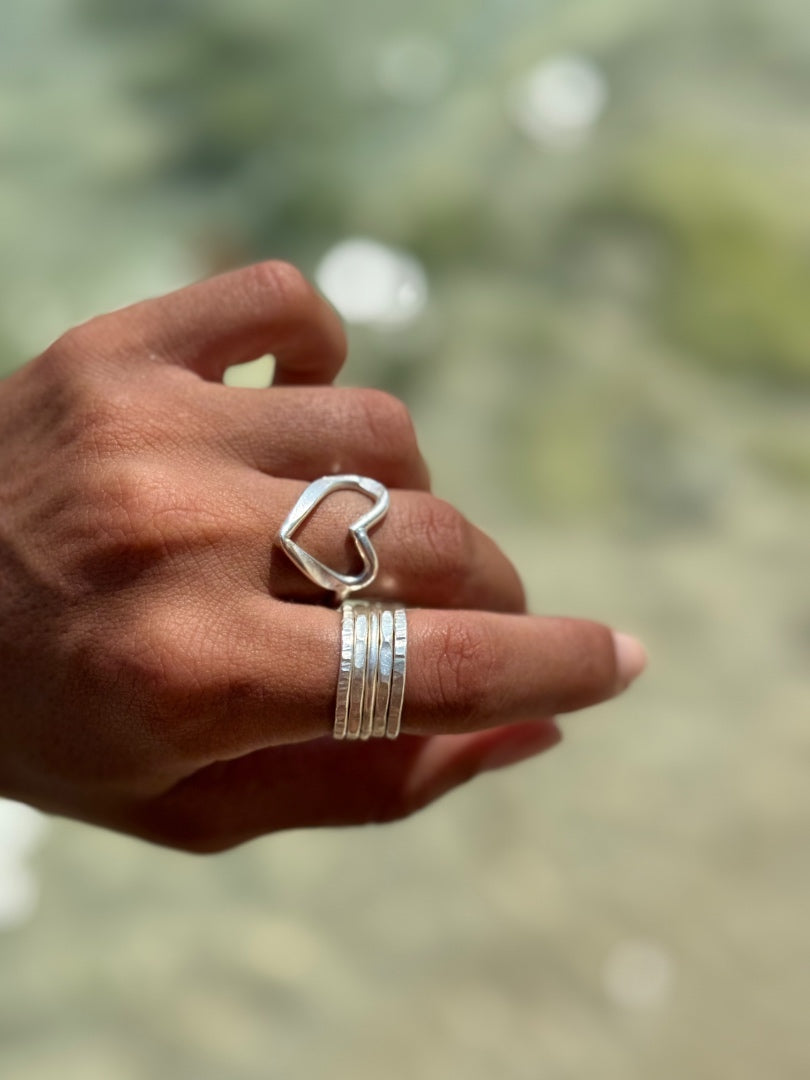 Hand wearing a silver heart-shaped ring with a blurred natural background
