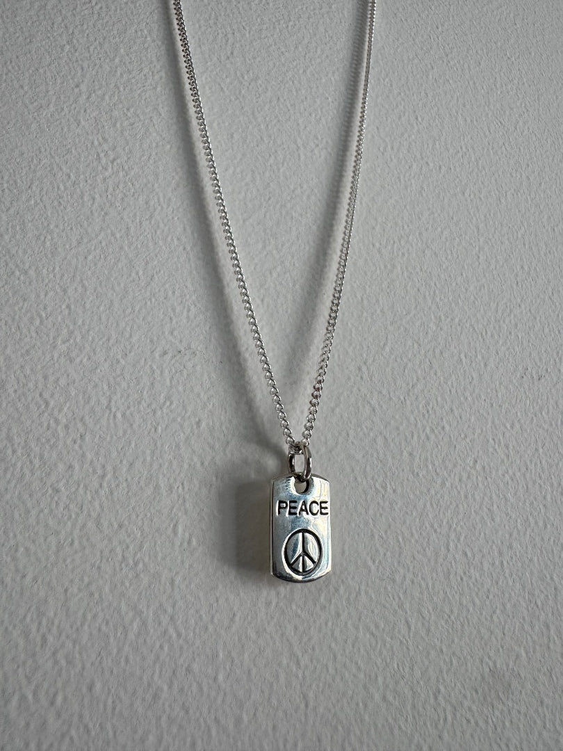 Silver necklace with a 'PEACE' pendant on a gray background
