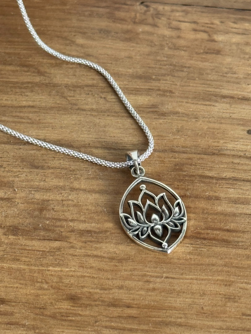 Silver lotus flower pendant necklace on a wooden surface
