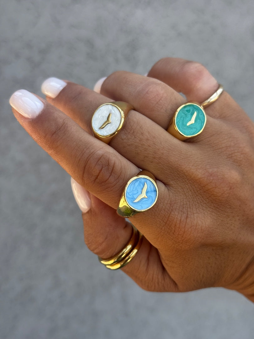 Hand wearing three rings with circular designs on a neutral background