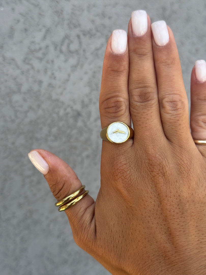 Hand wearing a gold ring with a circular design on a neutral background