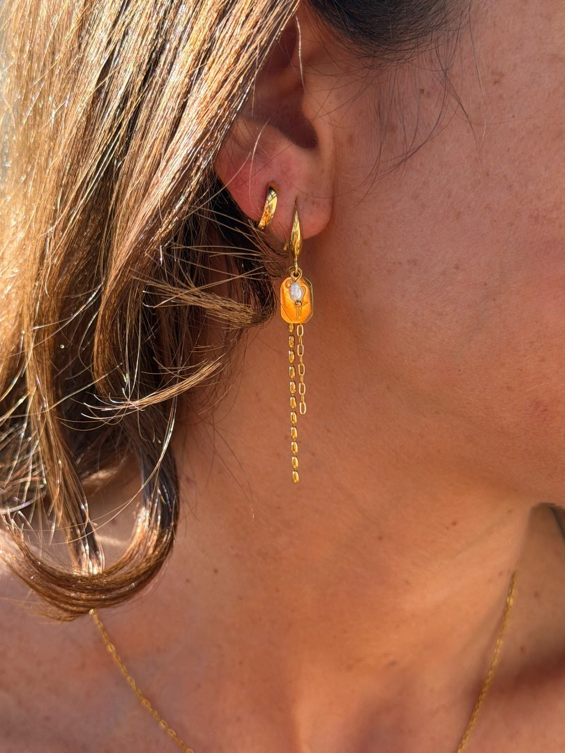 Close-up of a person wearing a gold earring with a chain and orange gemstone.