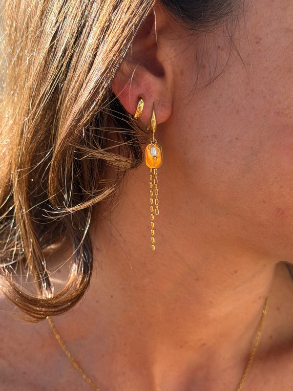 Close-up of a person wearing a gold earring with a chain and orange gemstone.