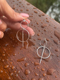 Silver earrings held by a hand on a wet wooden surface
