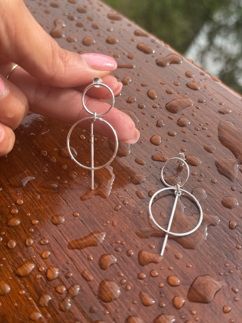 Silver earrings held by a hand on a wet wooden surface