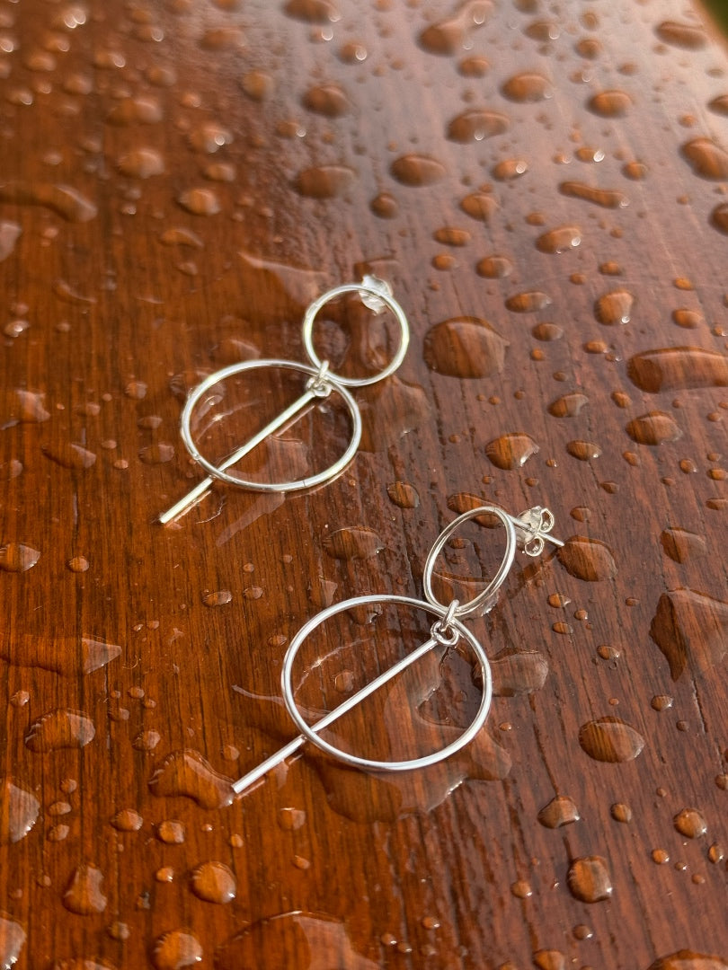 Silver earrings on a wooden surface with water droplets