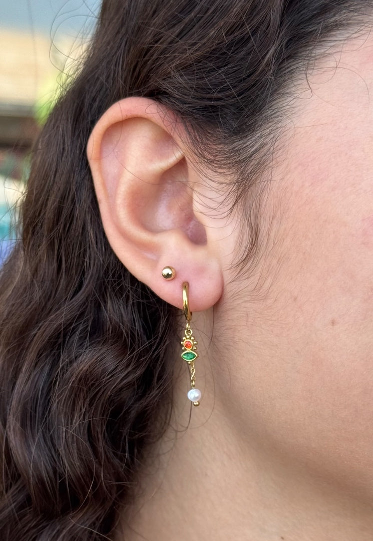 Close-up of an ear with a gold earring featuring a pearl and green gemstone.
