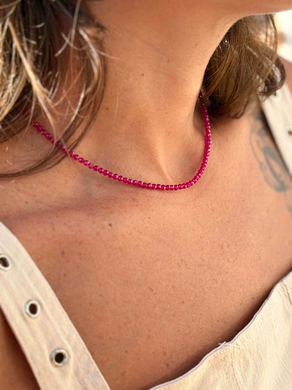 Close-up of a person wearing a pink beaded necklace with a neutral background
