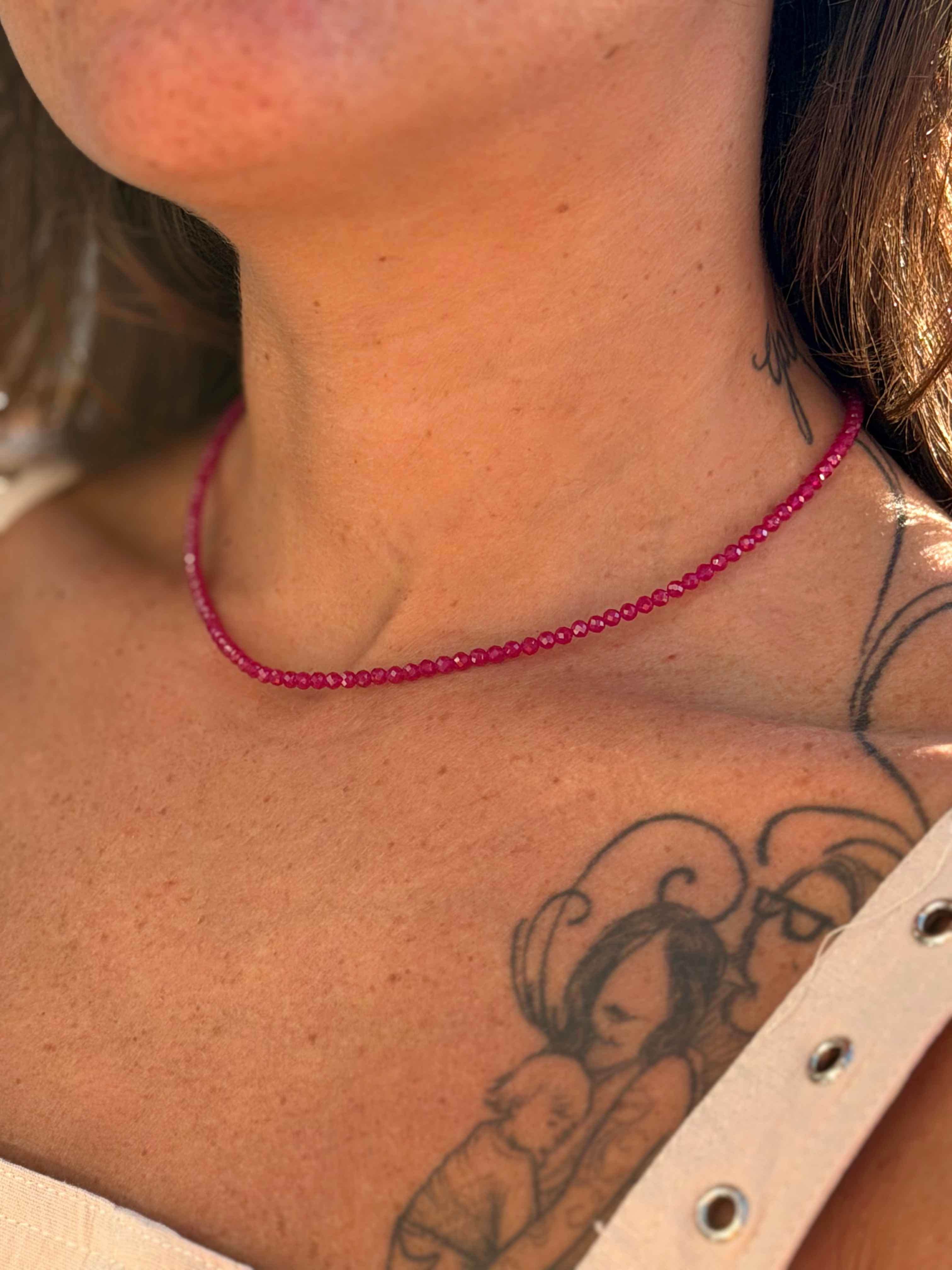 Necklace with pink beads worn by a person with tattoos on their neck and shoulder.
