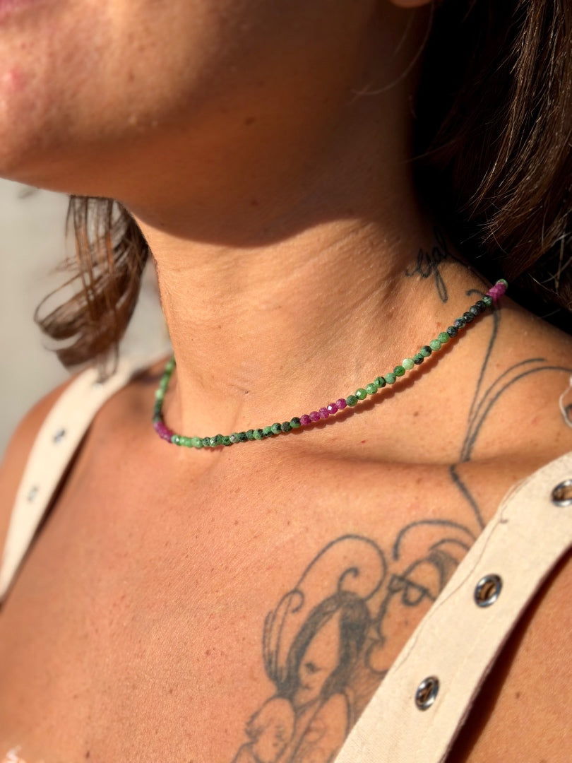 Person wearing a beaded necklace with green and pink beads, with tattoos on the neck and shoulder.
