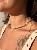 Person wearing a beaded necklace with green and pink beads, with tattoos on the neck and shoulder.