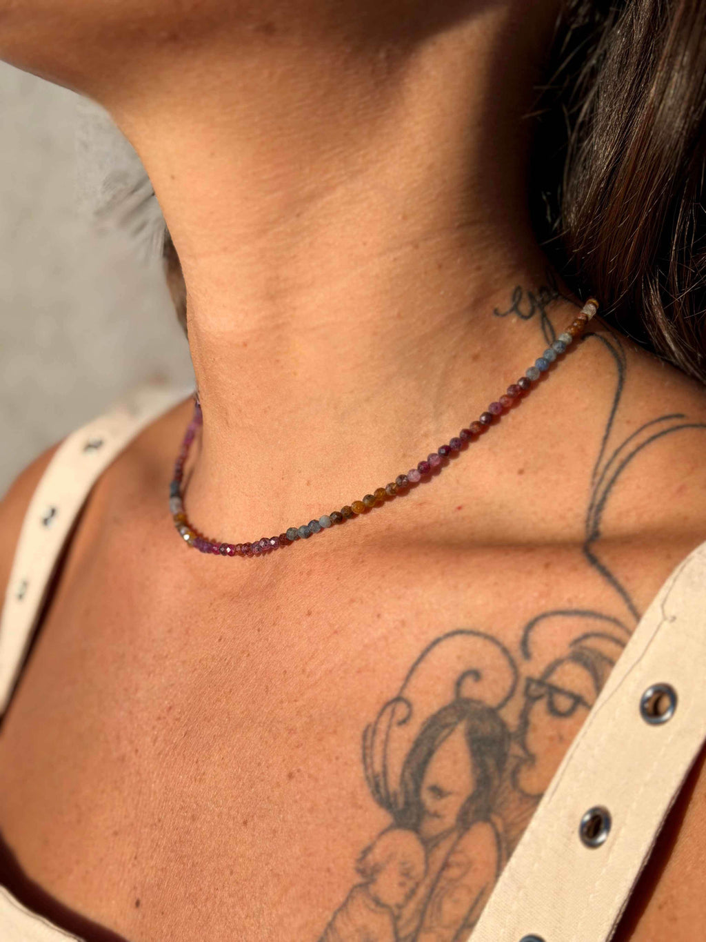 Close-up of a person wearing a colorful beaded necklace with tattoos on the neck and shoulder.