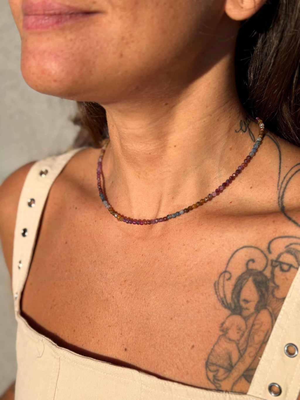 Close-up of a person wearing a beaded necklace with tattoos on their neck and shoulder.