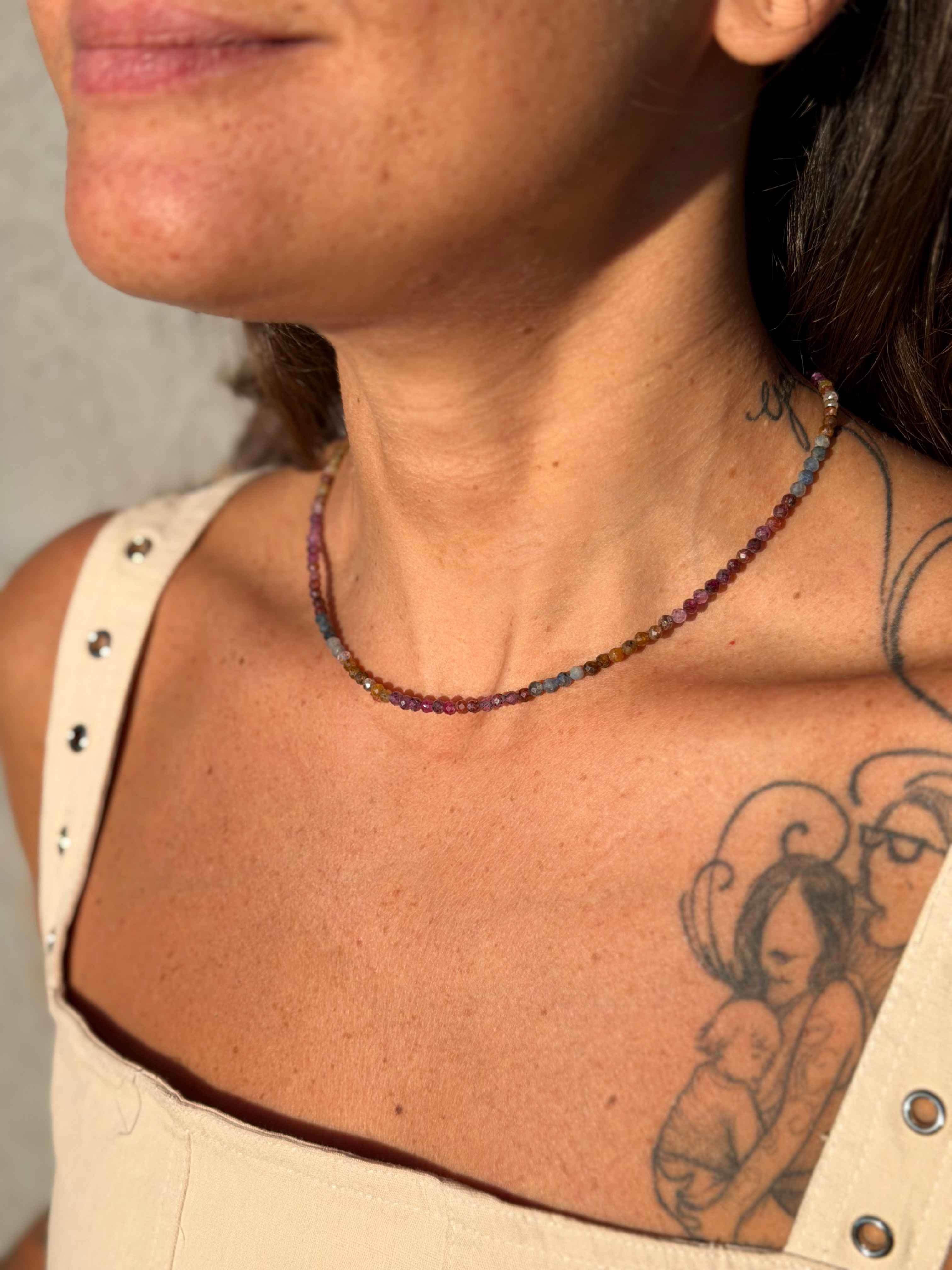 Close-up of a person wearing a beaded necklace with tattoos on their neck and shoulder.