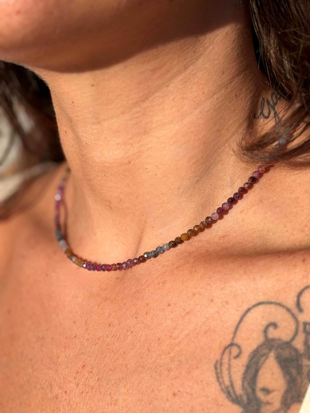 Close-up of a person wearing a multicolored beaded necklace with visible tattoos on the neck and shoulder.