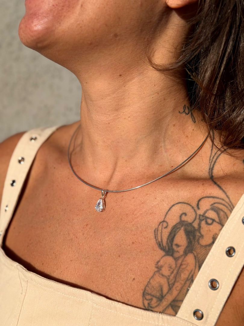 Close-up of a person wearing a necklace with a teardrop pendant, showing tattoos on the neck and chest.