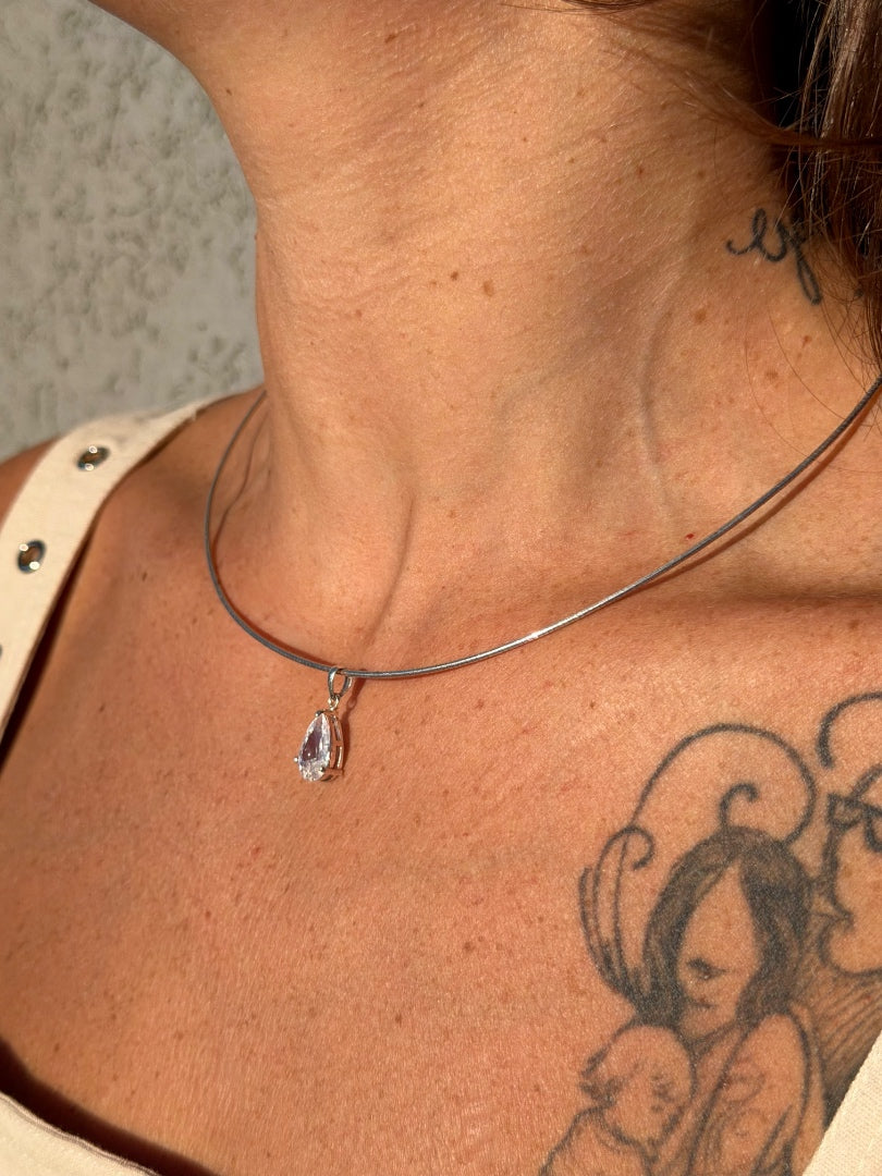 Necklace with a teardrop pendant worn by a person with tattoos on their neck and shoulder.