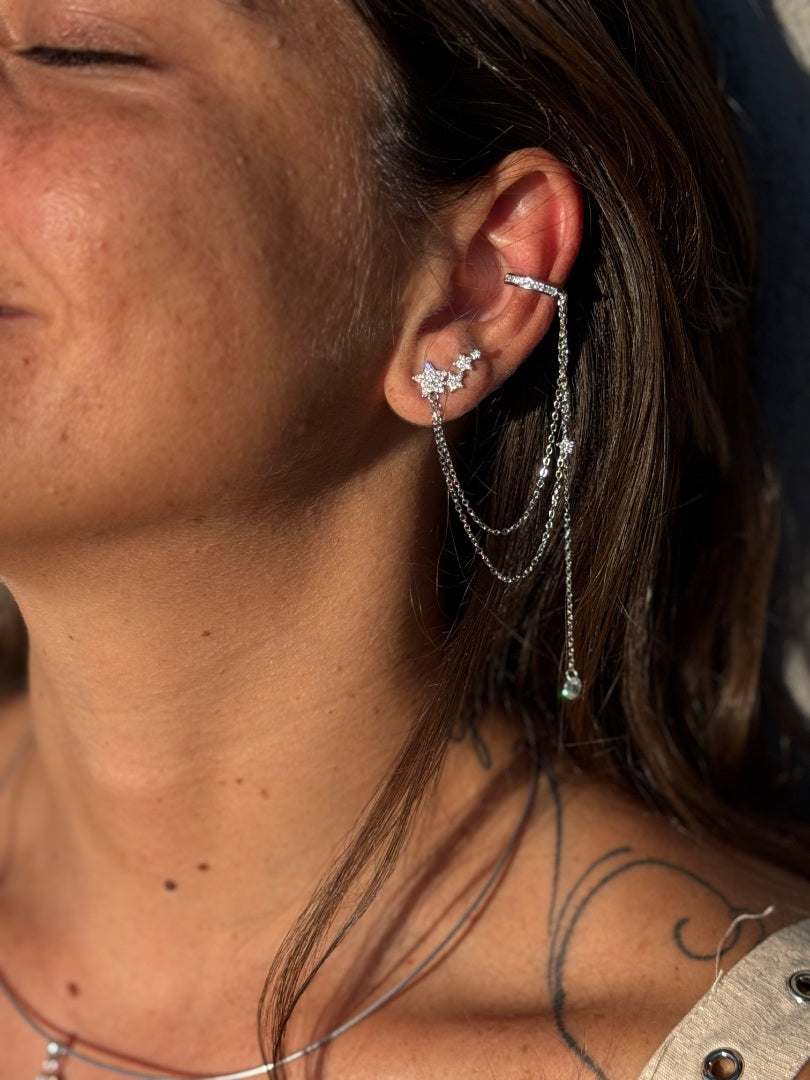 Close-up of a person wearing a star-shaped earring and a dangling chain earring.