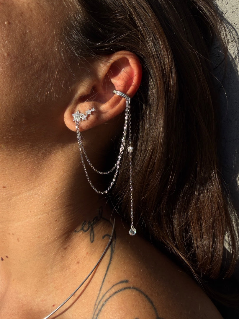 Close-up of an ear wearing a silver earring with dangling chains.