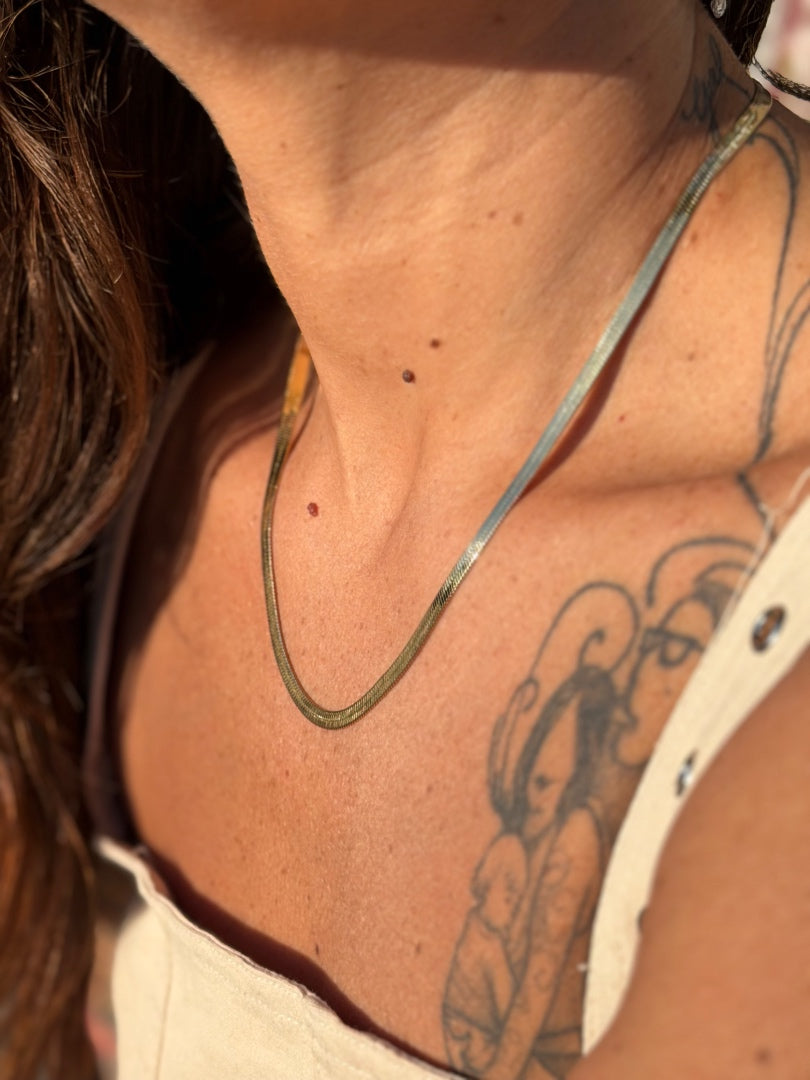 Close-up of a person's neck with a necklace and tattoo, sunlit background