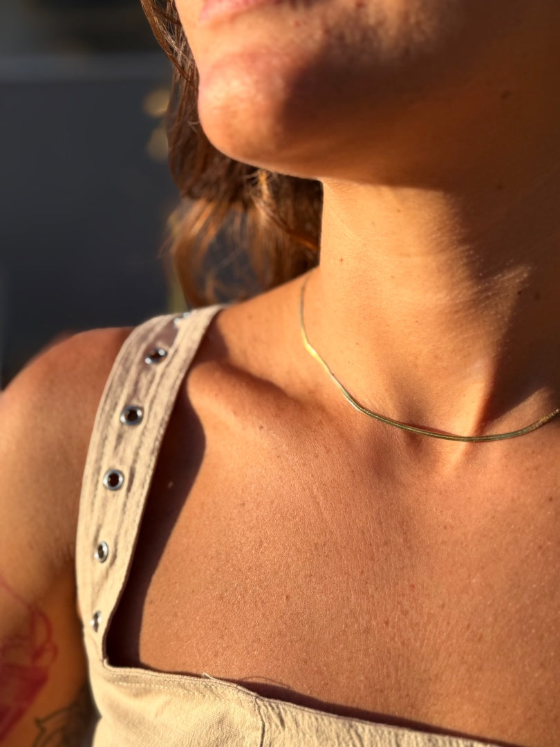Close-up of a person wearing a beige tank top and necklace with a blurred background