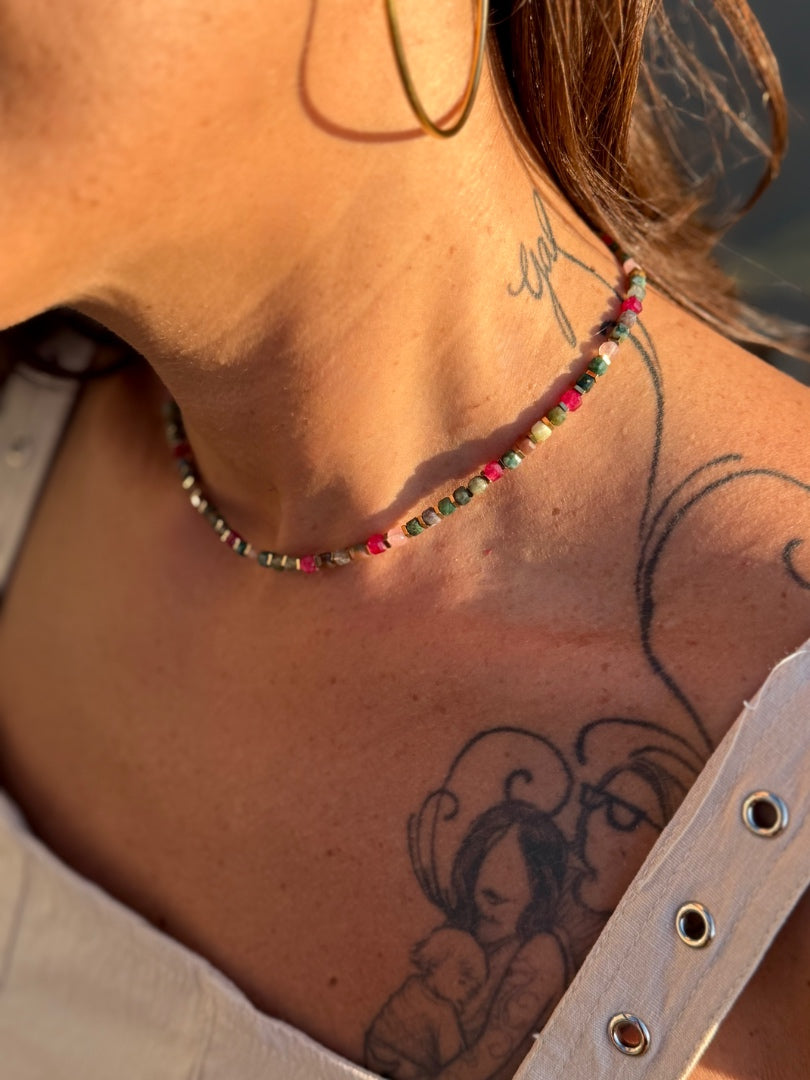 Close-up of a person wearing a colorful beaded necklace with tattoos on their neck.