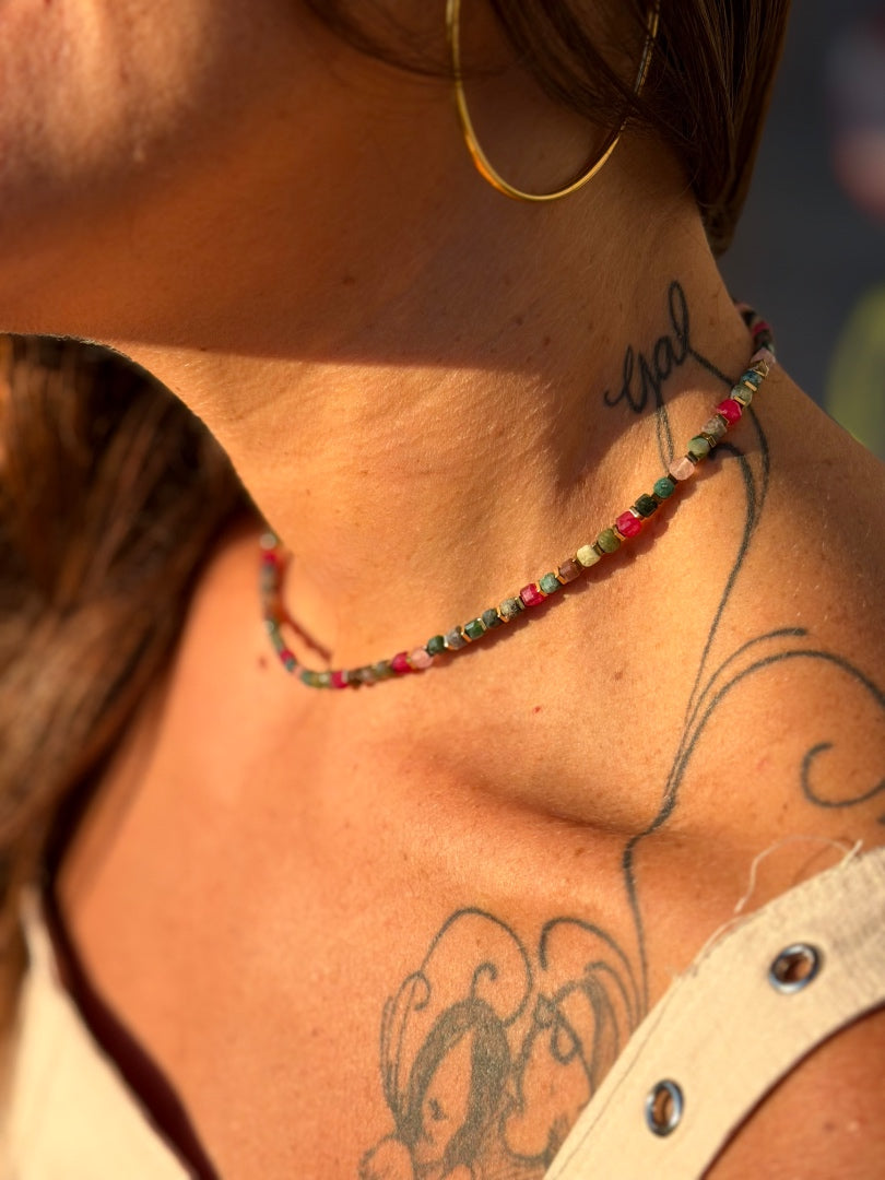 Close-up of a person's neck with a beaded necklace, tattoo, and blurred background