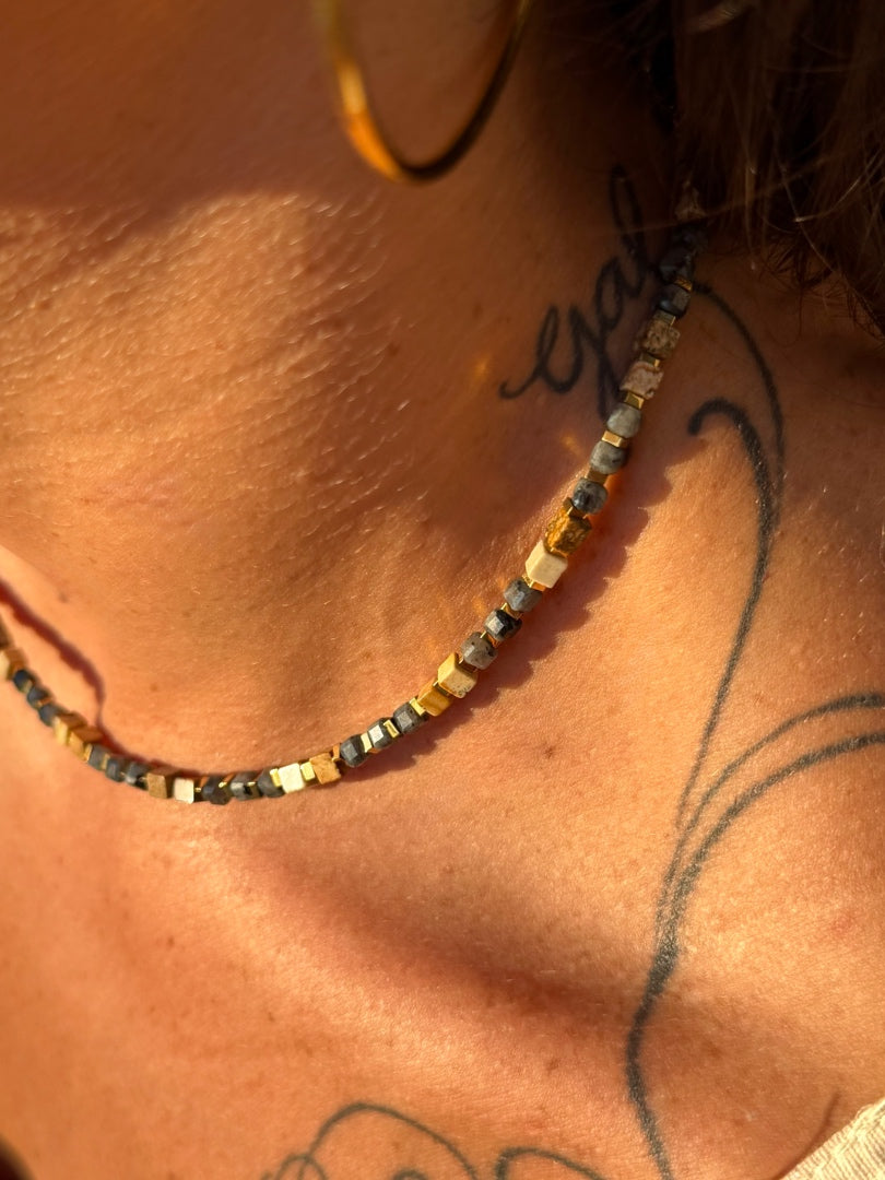 Close-up of a person wearing a beaded necklace with tattoos on the neck and shoulder.