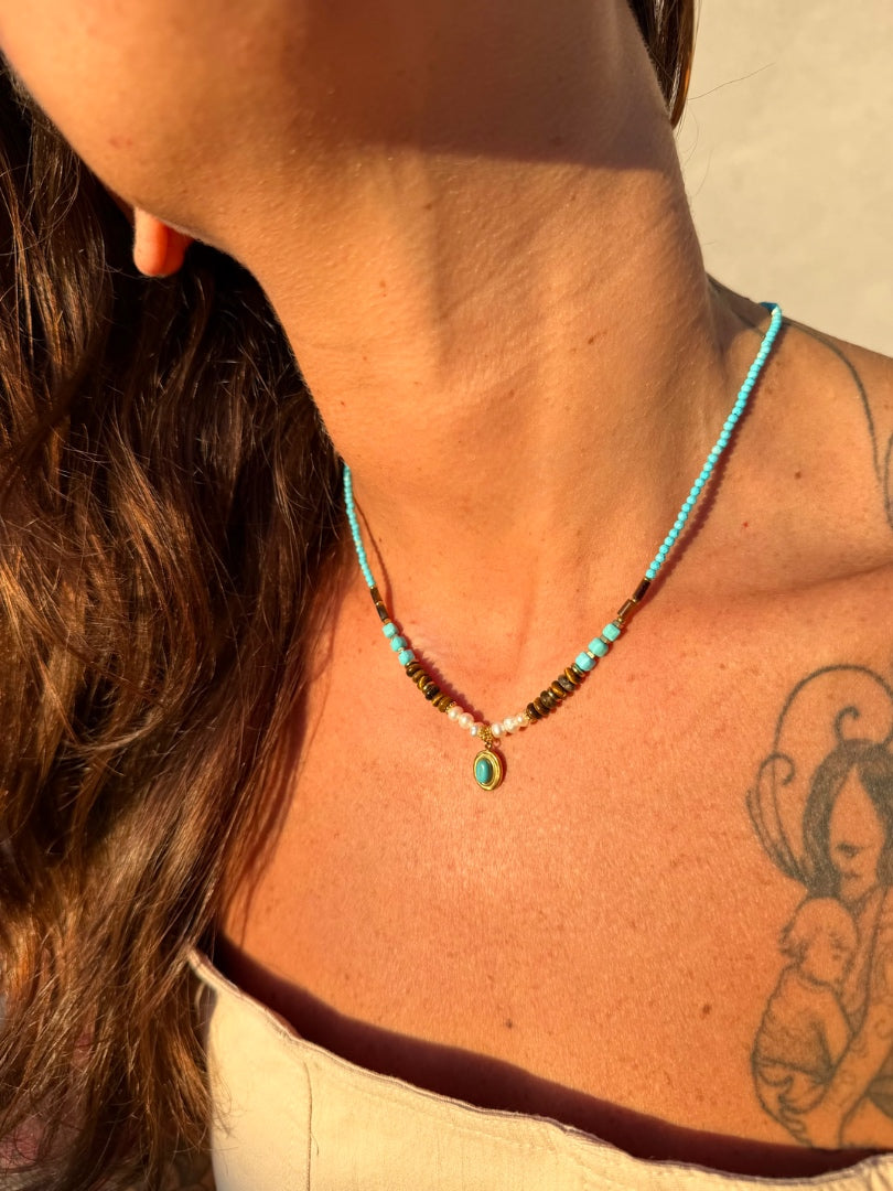 Close-up of a person wearing a turquoise beaded necklace with a tattoo on their shoulder.