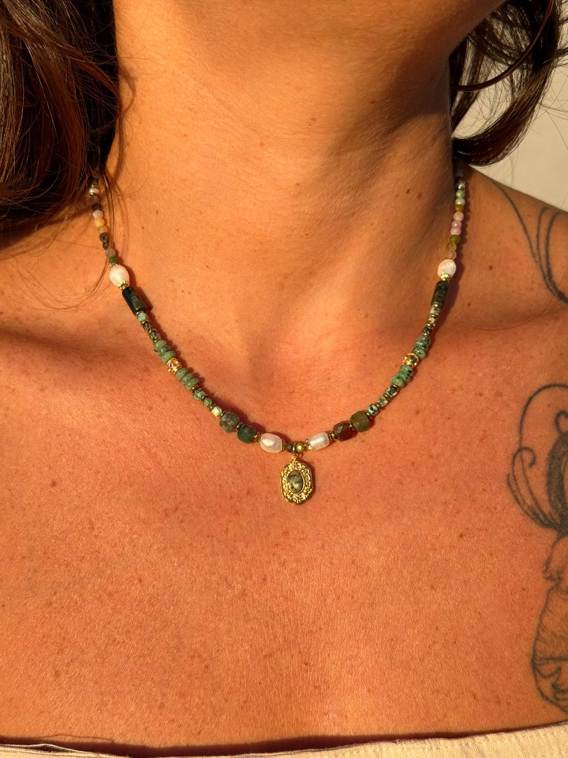 Necklace with green and gold beads worn by a person with a tattoo on their shoulder.