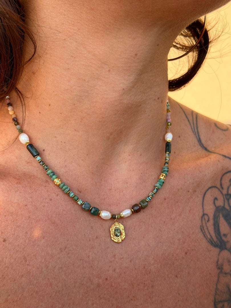 Necklace with green and gold pendant worn by a person with tattoos.