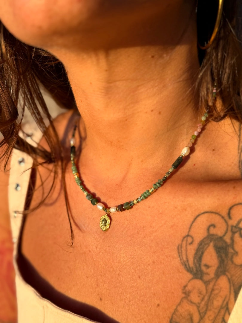 Necklace with green gemstones worn by a person with tattoos on their neck and shoulder.