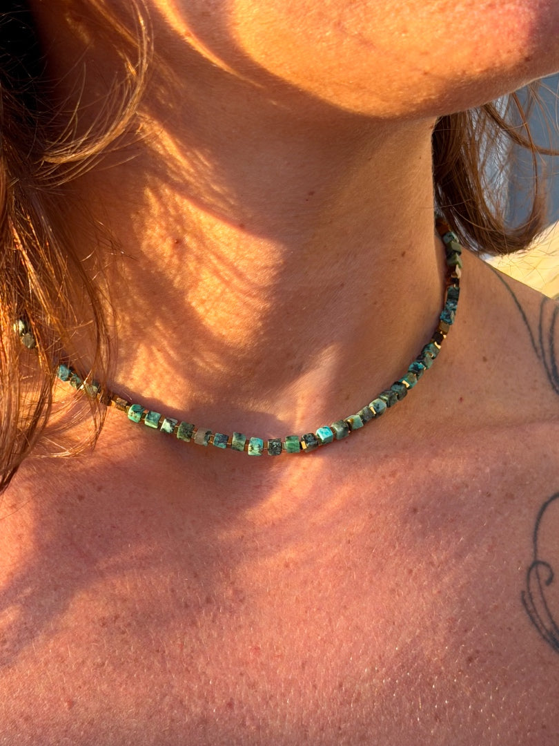 Close-up of a person wearing a green beaded necklace with sunlight casting shadows on their skin.