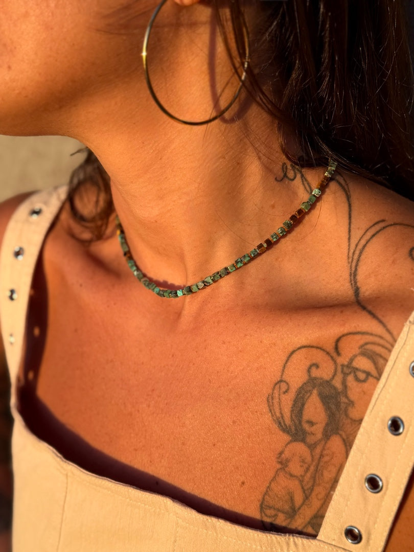 Close-up of a person's neck and shoulder with tattoos and a necklace.
