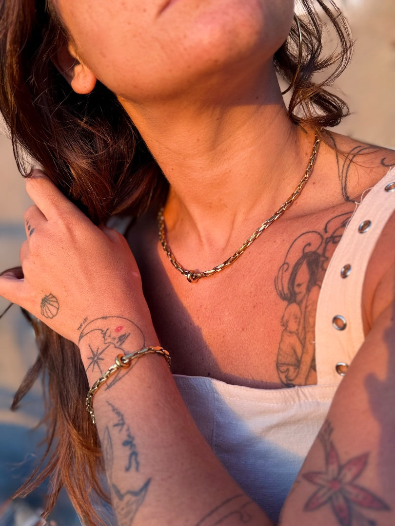 Close-up of a person with tattoos on their arm and neck, wearing a gold necklace and bracelet.