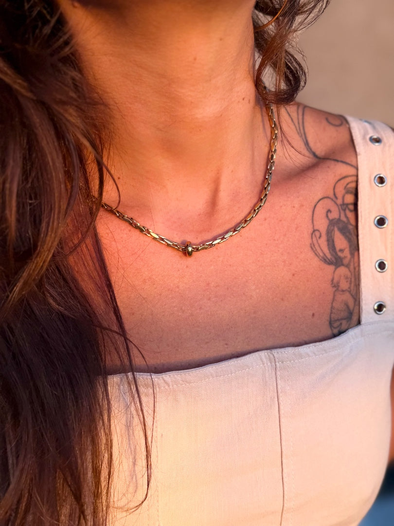 Close-up of a person with a tattoo on their shoulder wearing a gold necklace.