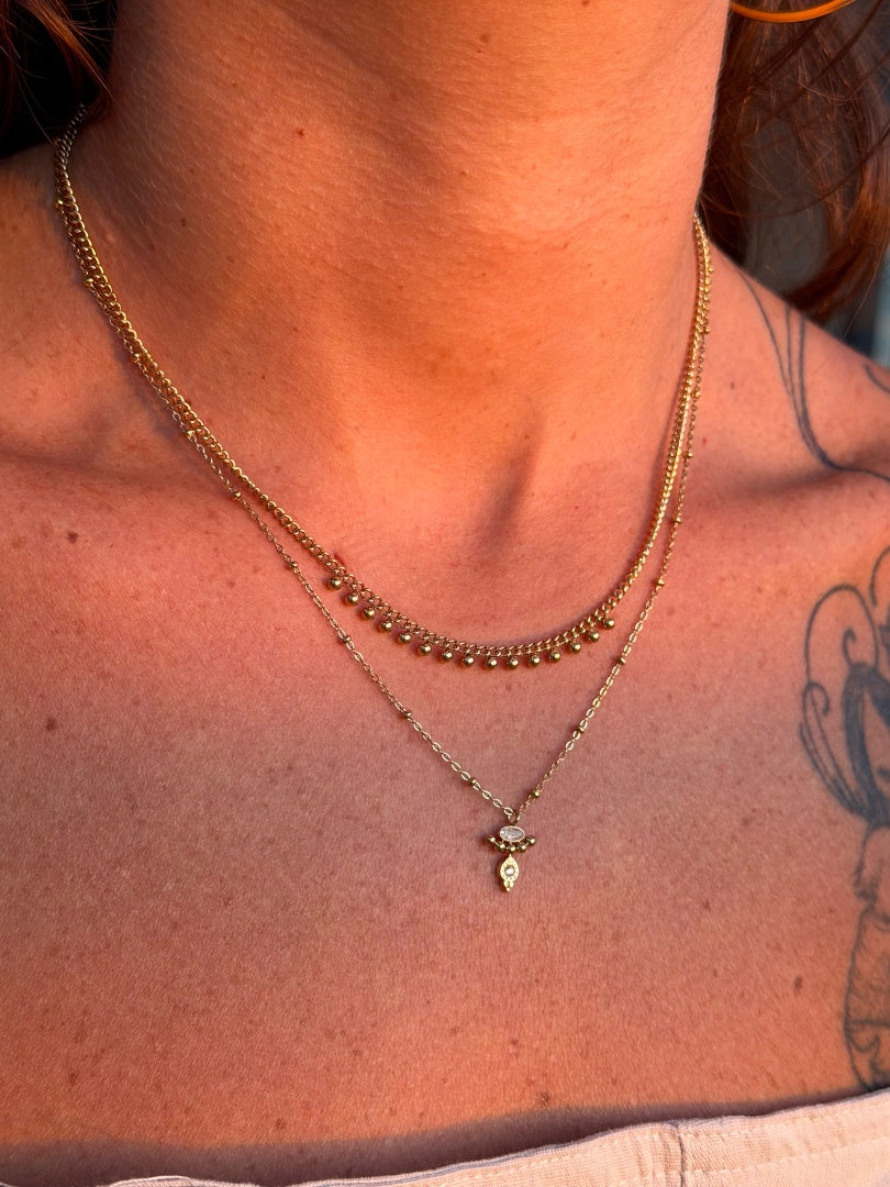 Close-up of a person wearing a gold necklace with a pendant, showing skin and a tattoo.