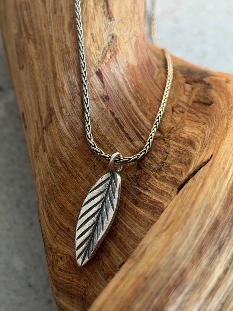 Silver leaf-shaped pendant on a chain against a wooden background