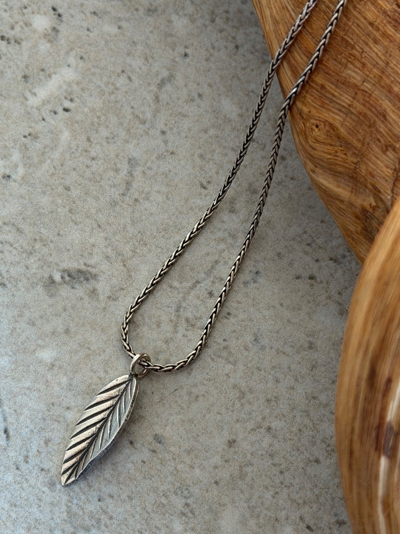 Silver feather necklace on a textured surface with wooden edge