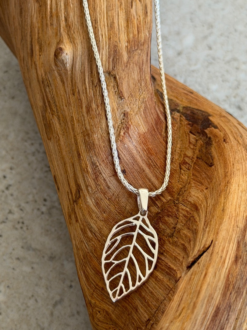 Silver leaf-shaped pendant necklace on a wooden surface