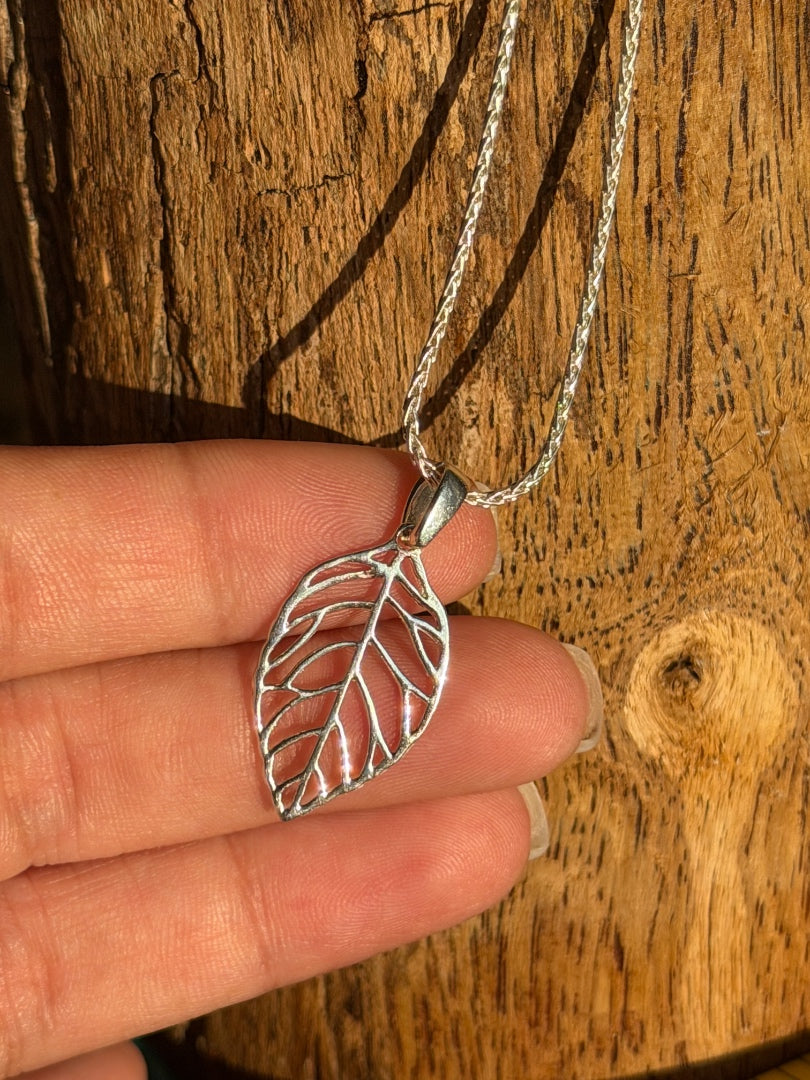 Silver leaf-shaped pendant on a chain held by a hand against a wooden background