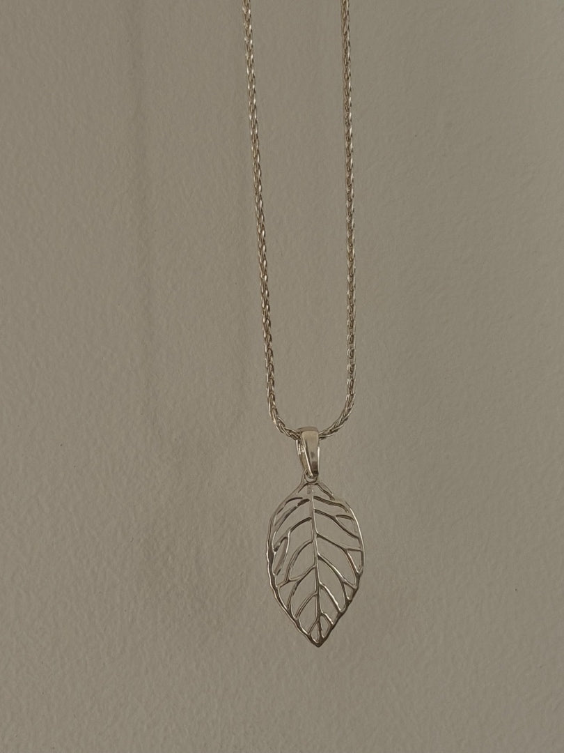 Silver leaf pendant necklace on a beige background