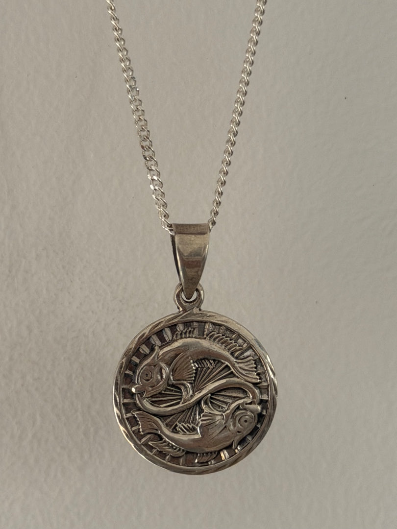 Silver pendant necklace with a detailed design on a plain background