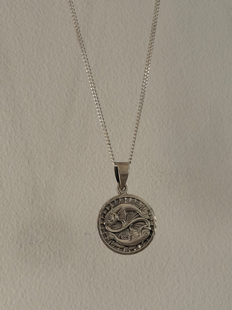 Silver necklace with a round pendant on a plain background