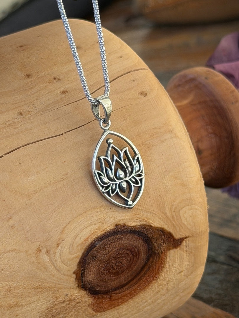 Silver lotus flower pendant on a chain, placed on a wooden surface