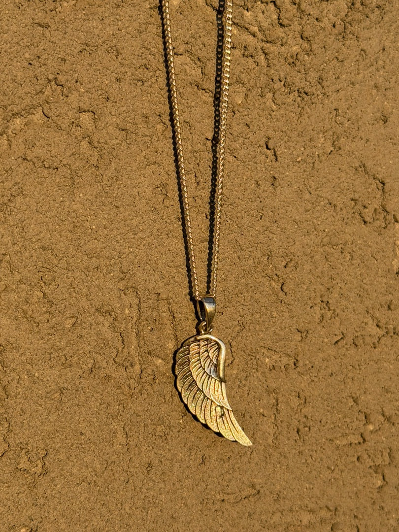 Gold wing-shaped pendant necklace on a textured brown surface