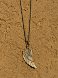 Gold wing-shaped pendant necklace on a textured brown surface
